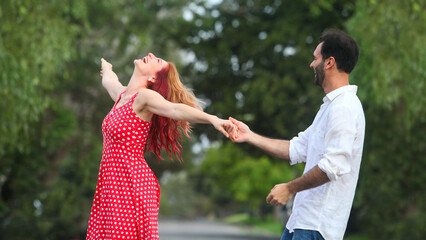 cheerful young man and woman dancing in park on summer day