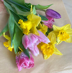 Beautiful composition of the first spring flowers with green leaves in a bouquet. Yellow daffodils, pink tulips in a bouquet on craft paper, top view.