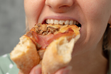 A close-up of a woman taking a bite of pizza with toppings.