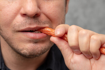 A close-up of a man biting a snack stick with a playful expression.