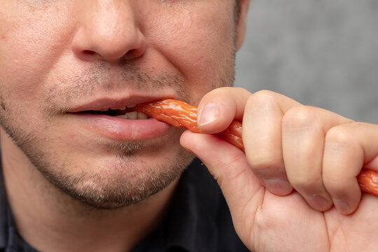 A close-up of a man biting a snack stick with a playful expression.