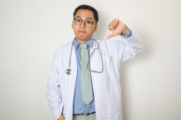 Young Chinese man as a medical doctor in studio showing a dislike gesture, thumbs down. Disagreement concept.