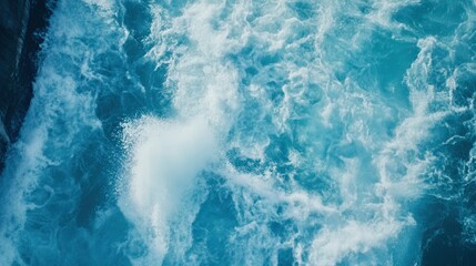 Fototapeta premium Turquoise ocean waves crashing against rocky shore under bright sunlight, creating foam