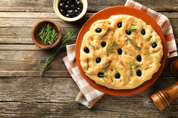 Delicious focaccia bread with olives, rosemary and spices on wooden table, flat lay. Space for text
