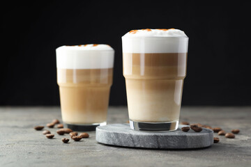 Tasty latte macchiato in glasses and coffee beans on grey table, closeup