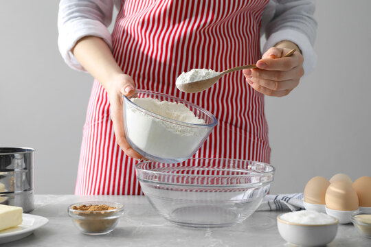 Making cinnamon rolls. Woman adding flour into bowl at gray marble table, closeup