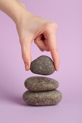 Woman making stack of stones on lilac background, closeup. Harmony and life balance