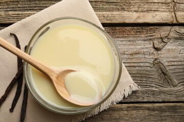 Tasty condensed milk, spoon and vanilla pods on wooden table, flat lay. Space for text