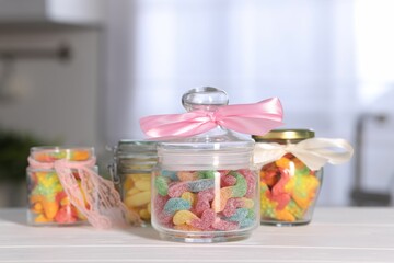 Tasty gummy candies in jars on light wooden table indoors