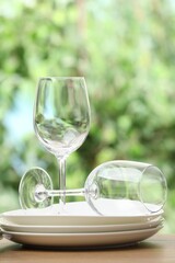 Clean dishware and glasses on wooden table against blurred green background