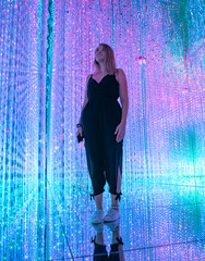 Young woman stands surrounded by colorful lights in an immersive art installation.