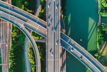 Aerial view of multiple highways intersect above a calm river, surrounded by vibrant greenery.