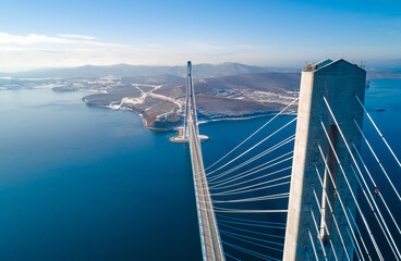 Fototapeta premium Aerial view of the cable-stayed bridge in Vladivostok, highlighting its towering pillars and cables against a backdrop of clear skies and calm waters