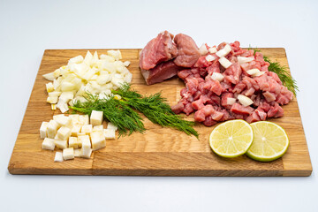 Fresh raw beef with vegetables and ingredients for cooking. Finely chopped meat, celery and onion on a wooden cutting board.