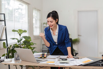 Excited businesswoman celebrating success while managing finances at her desk.