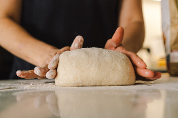 Hands are skillfully rolling and shaping dough on a clean kitchen countertop sprinkled with flour, healthy sourdough bread. The bright space suggests a cozy baking atmosphere.