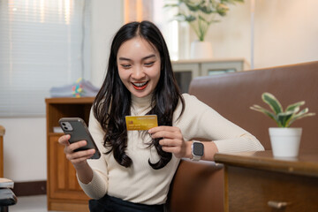 Happy asian woman making online payment using credit card and smartphone at home