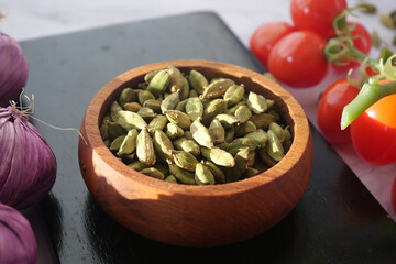 Cardamom pods in wooden bowl with fresh vegetables on table