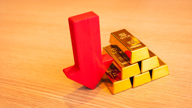 Gold bars and red arrow pointing down placed on the table, concept of gold price is decreasing due to going up high.