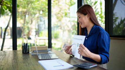 Businesswoman in a natural-themed office conducting a virtual meeting on a laptop, presenting...