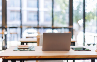 Laptop Computer, notebook, and eyeglasses sitting on a desk in a large open plan office space after working hours	