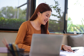 Businesswoman analyzing documents at a natural-themed office with a laptop, focused and dedicated to her work.