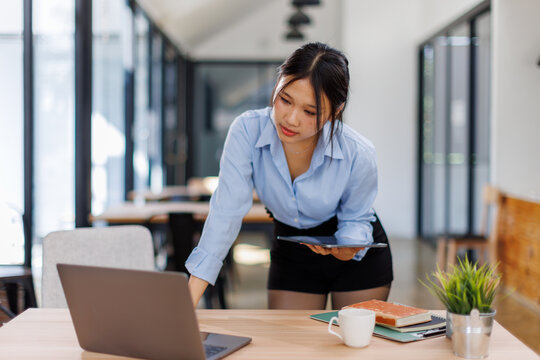 Female asian business person using digital tablet and laptop or remote working at office, looking at digital tablet watching webinar, learning training, studying online seminar or video calling.
