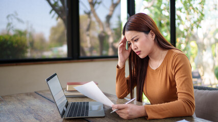 Businesswoman analyzing documents with a stressed expression in a natural-themed office, dealing with work challenges.