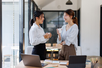 Two Cheerful asian Business women standing in the workplace office and discussing their ideas
