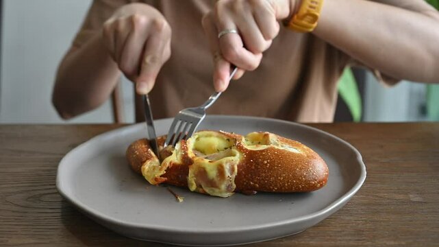 Someone cutting a slice of sausage cheese pretzel bun for eat. Pretzels are a type of bread typically made from wheat or rye flour