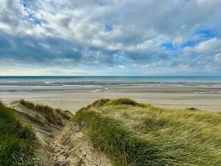 Stunning Authie Bay coastal view from the dunes overlooking a vast sandy beach, tidal pools, and the open sea under a dynamic cloudy sky, with wind-swept dune grass framing the scenic landscape