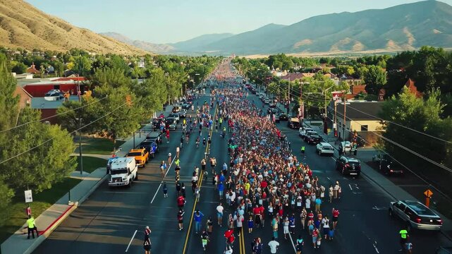 Crowded Independence Day parade on Provo Street with mountains in the background during daylight, Independence day parade on provo street - high, drone shot