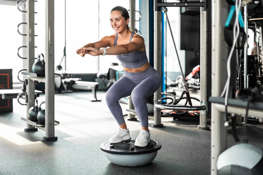Sporty woman making squats on balance trainer.