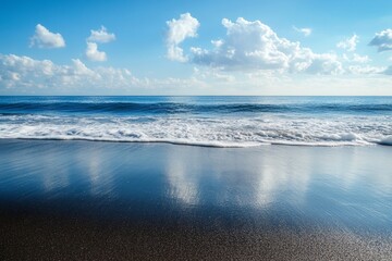 Obraz premium A stunning view of a tranquil ocean with gentle waves lapping against the shore. Fluffy clouds drift in the bright blue sky, creating a serene atmosphere.