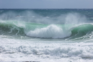 A wave driven by an approaching cyclone or hurricane crests and crashes in the middle in rough surf with wind driven spray at Snapper Rocks at Coolangatta on the Gold Coast in Queensland, Australia.