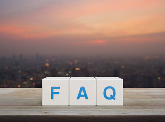 FAQ acronym on white block cubes on wooden table over blur of cityscape on warm light sundown,...