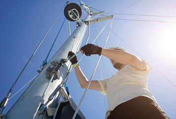 Male captain on deck of sailboat opening sails pulling the rope