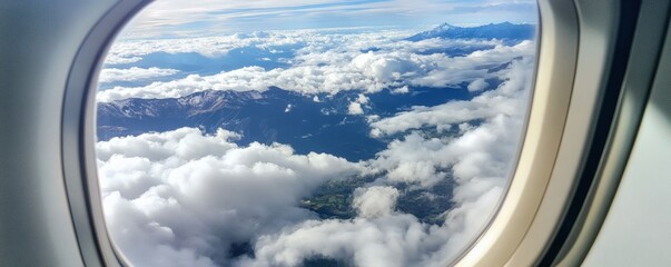 The plane window reveals majestic mountains and fluffy clouds in the sky