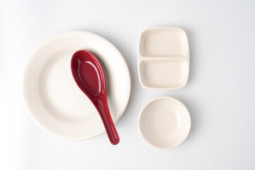 Empty beige colored round shaped plate, dual dipping bowl and red colored chinese soup spoon....