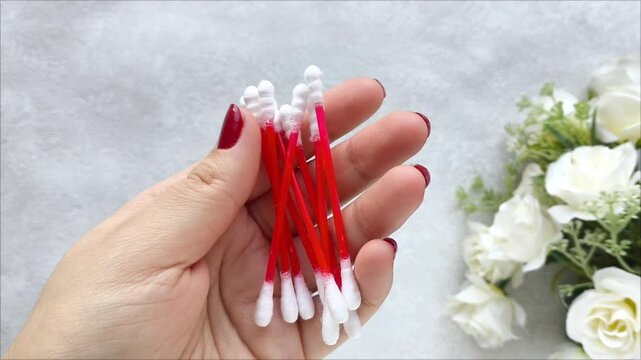 Plastic disposable cotton swabs in a woman's hand on a gray background. Hygienic cotton swabs for cleaning ears. 