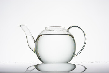 Teekanne aus Glas vor weißem Hintergrund ohne Deckel, gefüllt mit farbloser Flüssigkeit bzw....