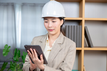 Asian project manager or architect female using digital technology tablet assigning work checking report writing letters to customers or employees, start-up young engineer woman working at home office