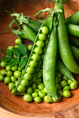 Top view of green sugar snap peas with open pods in rustic wooden plate close up. Green pea beans vegetables. Food photography