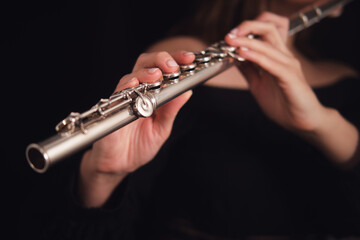 Musician's hands holding and playing a silver flute on a dark background. Studio music photography....