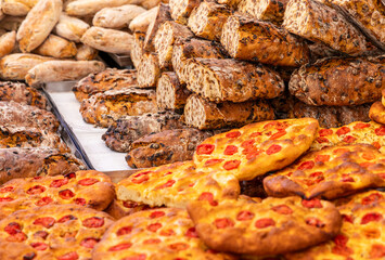 Traditional Italian street market stall with rustic raisin bread crispy tomato focaccia and fresh olive bread stacked and displayed for customers and visitors at a food fair