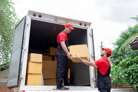 Indian and Caucasian partnership mover workers in red uniform uploading furniture and boxes to new house, shipping company small business owner using delivery truck sending packages to customers