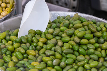 Green olives preserved in brine at an Italian market with a plastic scoop resting in the container