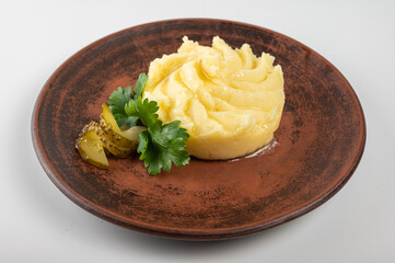 Creamy mashed potatoes with melted butter on a rustic plate, garnished with pickles and fresh parsley. A delicious side dish perfect for homemade meals and comfort food lovers