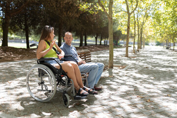 Young woman in wheelchair talking with friend in park