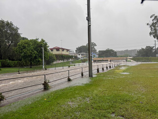  Flooded urban area with murky water overflowing near a walkway and railing during heavy rain at...
